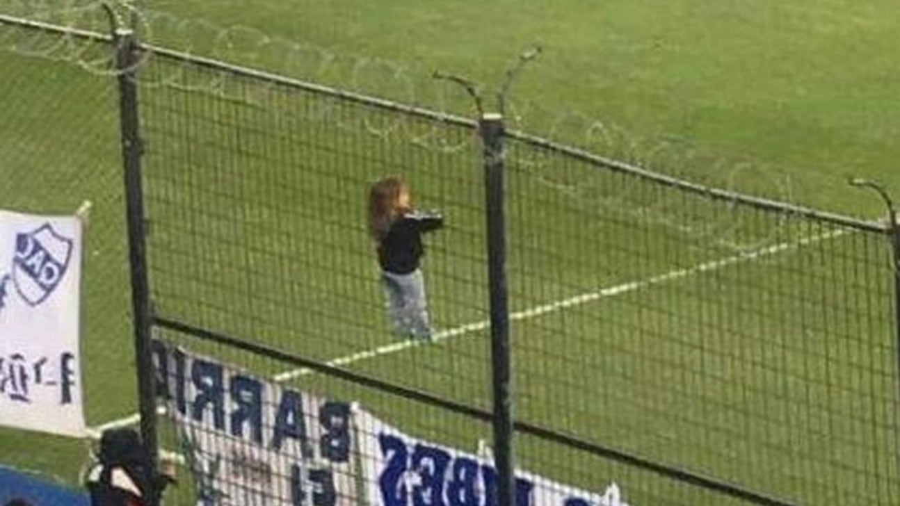 This is a small child climbing a barbed wire fence to watch an Argentine soccer match