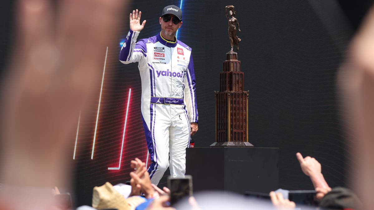 Denny Hamlin waves as he is introduced during the pre-race driver introductions before the start of the NASCAR Cup Series FireKeepers Casino 400