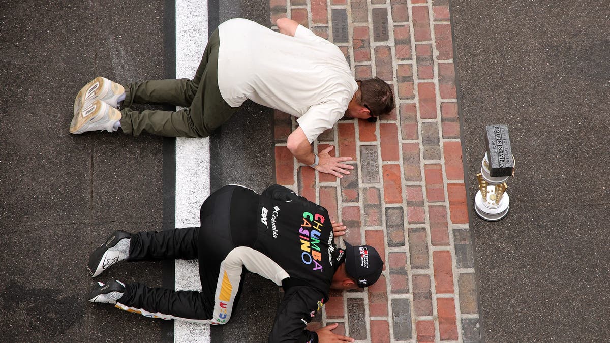 Bubba Wallace and Denny Hamlin, co-owner of 23XI Racing, kiss the yard of bricks after winning the NASCAR Cup Series Brickyard 400