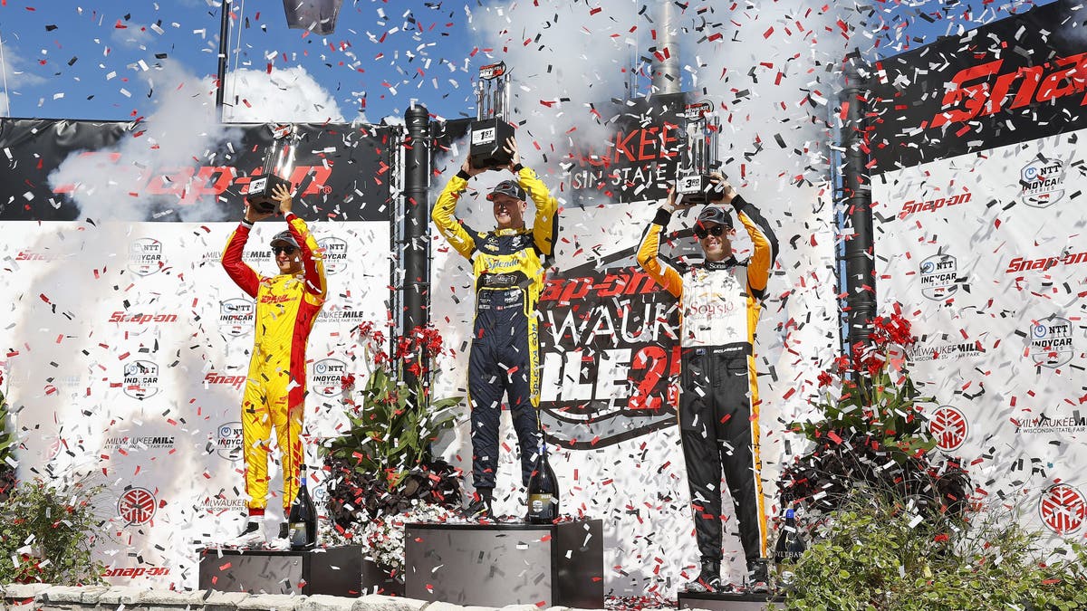 Christian Rasmussen (center), Alex Palou (left) and Scott McLaughlin in victory circle on the podium during the NTT INDYCAR Series Snap-On Milwaukee Mile 250.