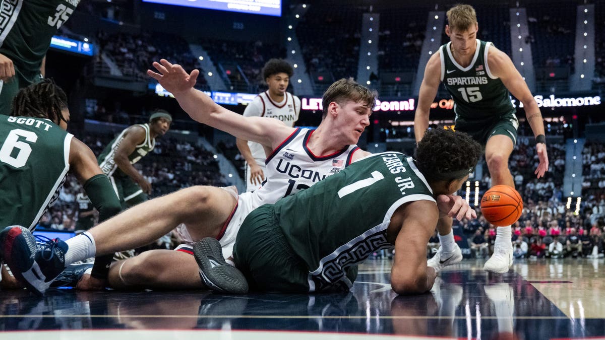 Eric Reibe #12 of the Connecticut Huskies and Jeremy Fears Jr. #1 of the Michigan State Spartans go for the loose ball during the second half of an NCAA men's basketball exhibition. (Photo by Joe Buglewicz/Getty Images)